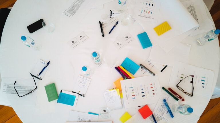 Table with papers, notes, pens and other writing stationary, water bottles, and more