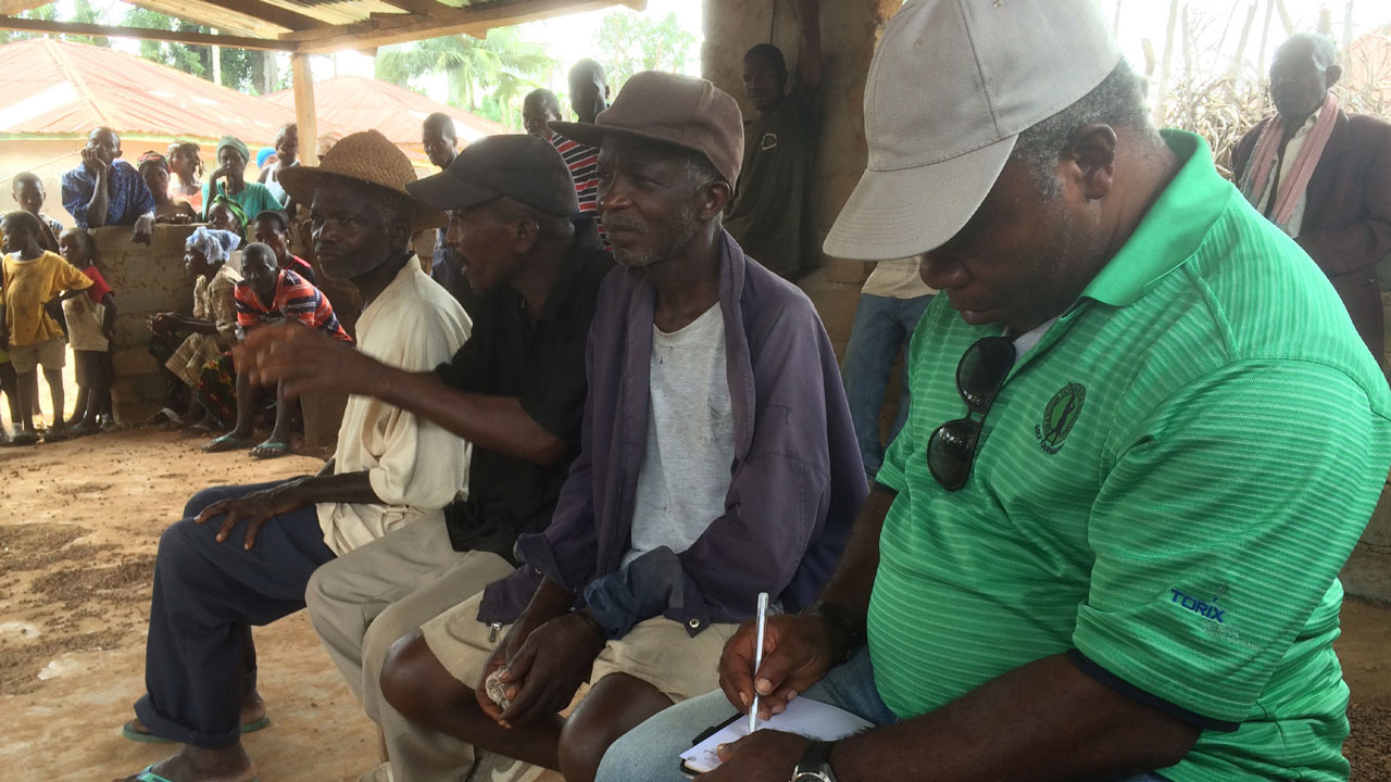 Meeting four men sitting on a bench, one man in green shirt taking notes