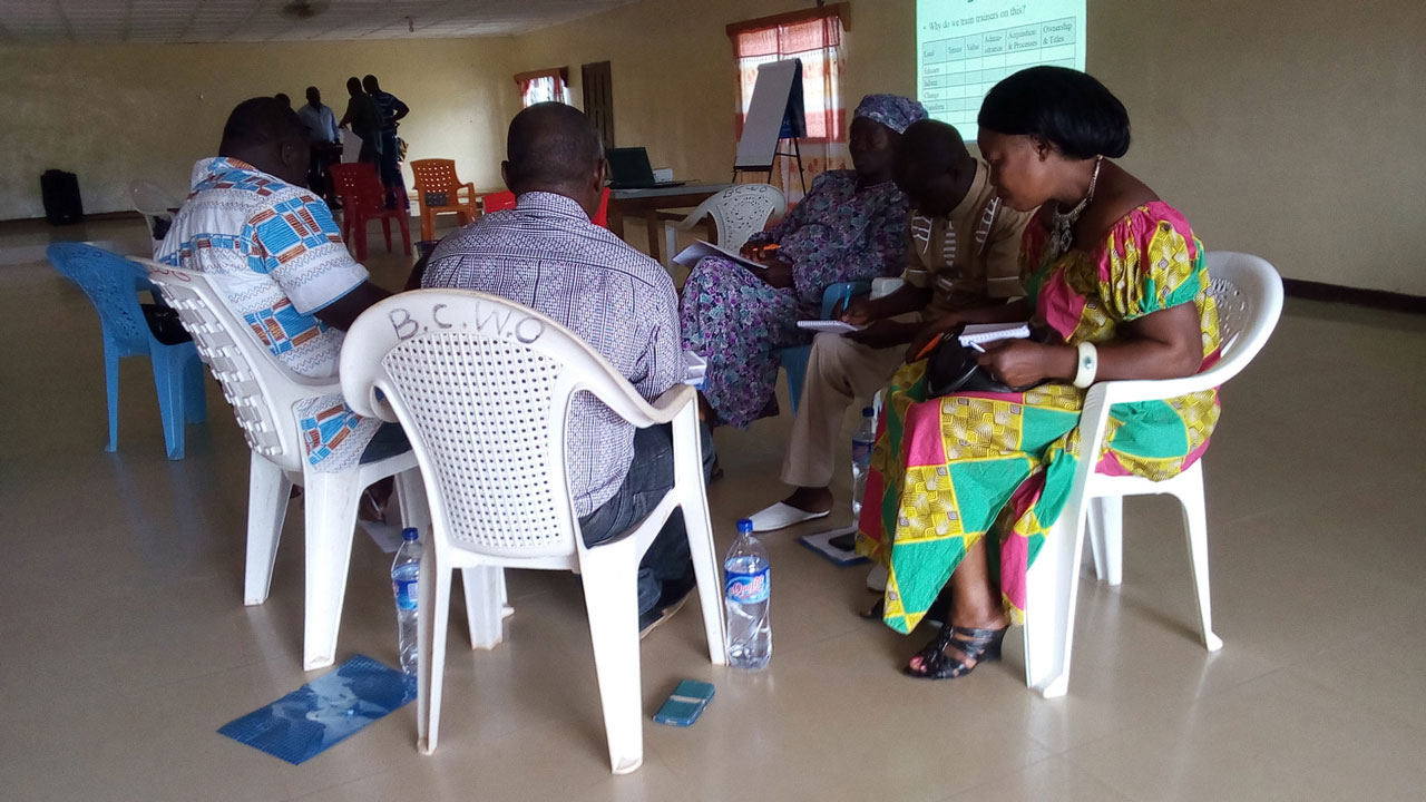 Men and women sitting in chairs in a circle taking notes