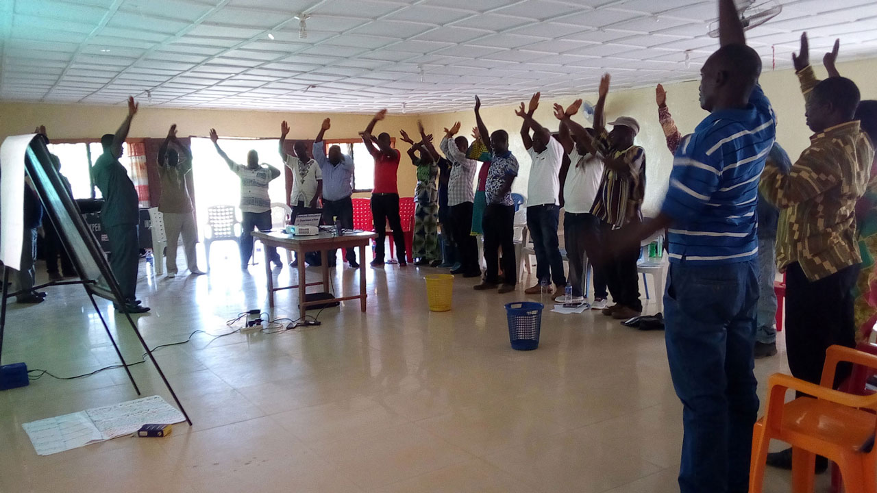 Training workshop participants standing in semi-circle with right hands raised