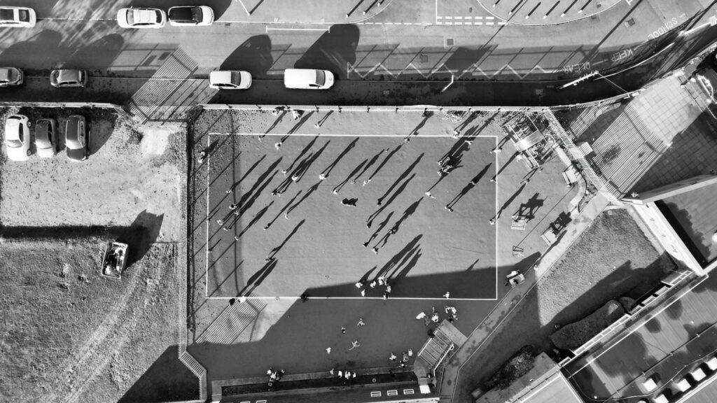 A group of people scattered across a field in a commercial area, next to a busy street