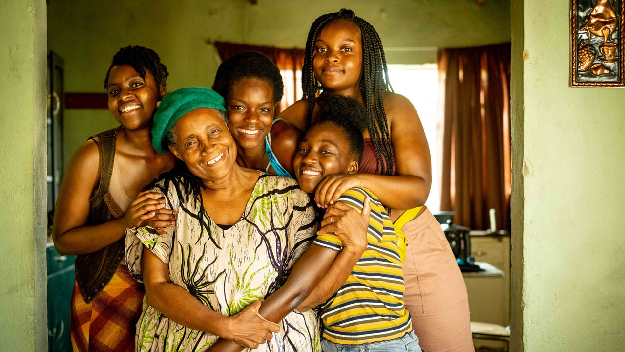 Four young women smiling and hugging an elderly woman