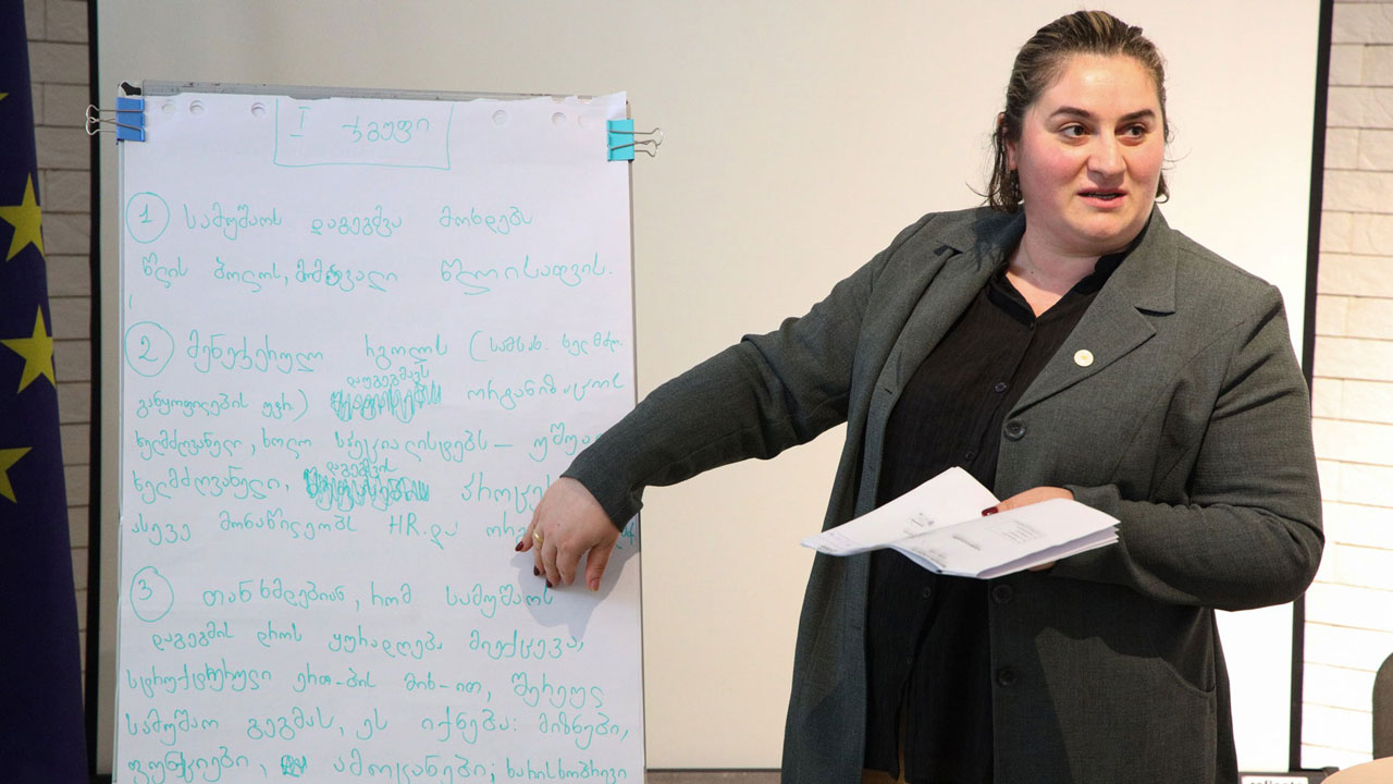 Presenter standing at the white board at workshop on HR performance appraisal system modeling