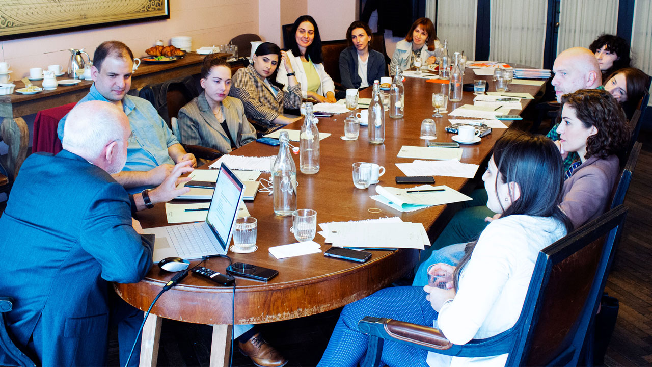 Participants sitting around a conference table in a workshop on how to develop best practices for projects