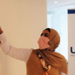 Woman wearing facemask pointing at collage with USAID banner in the background