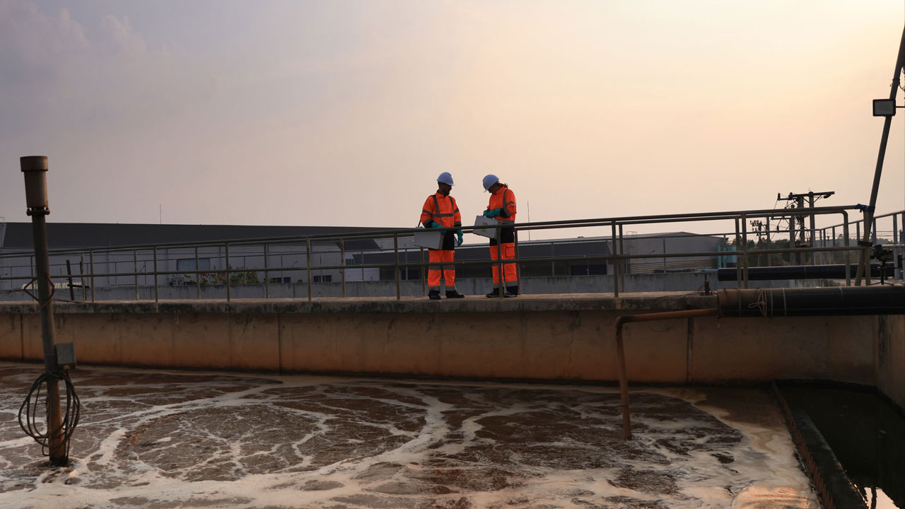 Two engineers are inspecting the water treatment system by standing on the bridge at sunset