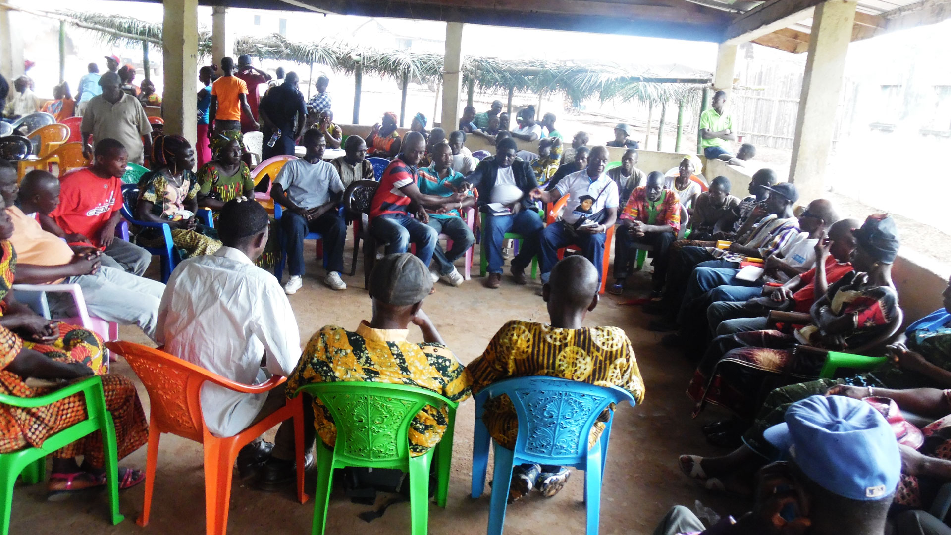 Community members sitting and standing in a circle in a meeting