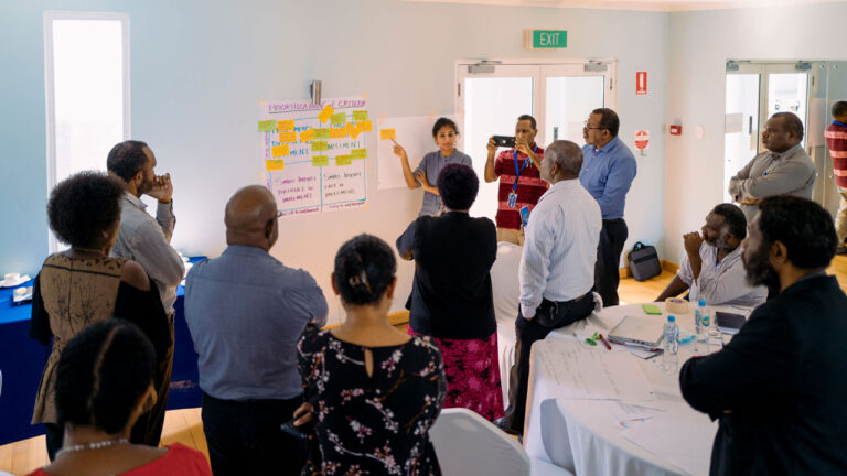 Workshop lead by staff member to an audience who are standing and looking at annotated poster